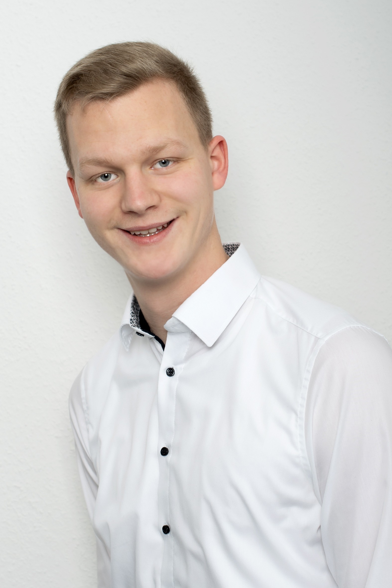 Finn Westermann, ein junger Mann mit blonden Haaren und blauen Augen, lächelt in einem weißen Hemd mit schwarzen Knöpfen.
